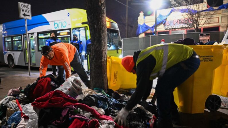 Trabajadores de saneamiento limpian una pila de mantas y ropa usadas junto a un campamento de migrantes cerca de una estación de autobuses en el centro de El Paso, Texas, donde esperaban transporte para refugiarse al cruzar la frontera entre Estados Unidos y México el 17 de diciembre de 2022. (PATRICK T. FALLON/AFP vía Getty Images)