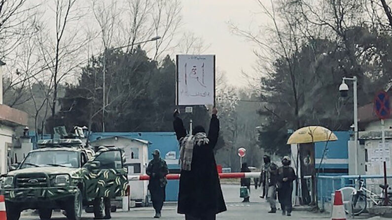 Esta fotografía tomada el 25 de diciembre de 2022 muestra a la estudiante Marwa protestando en solitario contra la prohibición de la educación superior a las mujeres, frente a la Universidad de Kabul mientras miembros de los talibanes montan guardia en Kabul. (AFP vía Getty Images)