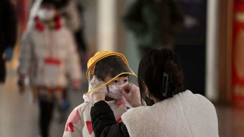 A woman arranges a face mask on a child's face in a departure terminal of the international airport in Beijing on December 29, 2022. - China announced this week that incoming travellers would no longer have to quarantine from January 8, the latest major reversal of strict restrictions that have kept the country largely closed off to the world since the start of the pandemic. (Photo by Noel Celis / AFP) (Photo by NOEL CELIS/AFP via Getty Images)