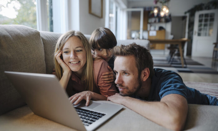 Una familia acostada en el sofá usando una computadora portátil. (Westend61/Getty Images)
