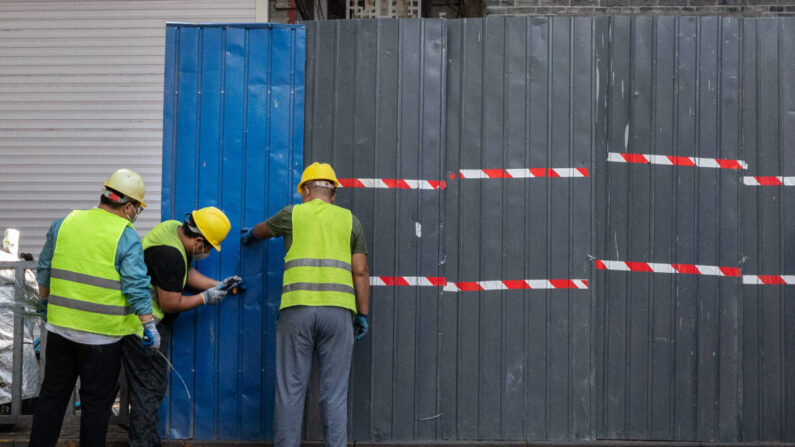 El 23 de junio de 2022, en el distrito comercial de Sanlitun, en Beijing (China), unos trabajadores levantan una valla alrededor de las residencias y comercios locales en cierre tras detectarse nuevos casos locales de COVID-19. (Kevin Frayer/Getty Images)
