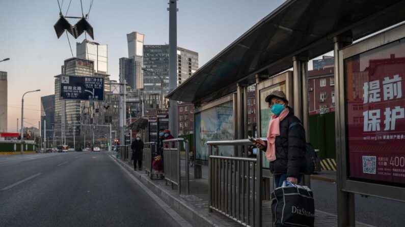 Una mujer lleva una mascarilla para protegerse de la propagación del COVID-19 mientras espera en una parada de autobús en una calle habitualmente concurrida del Distrito Central de Negocios el 6 de diciembre de 2022 en Beijing, China. (Kevin Frayer/Getty Images)