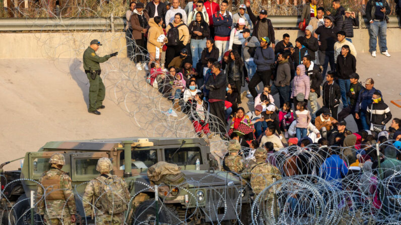 El agente de la Patrulla Fronteriza habla con unos migrantes mientras les bloquea el ingreso a un área de cruce fronterizo ilegal de alto tráfico a lo largo de Río Grande en El Paso, Texas, el 20 de diciembre de 2022, visto desde Ciudad Juárez, México. (John Moore/Getty Images)