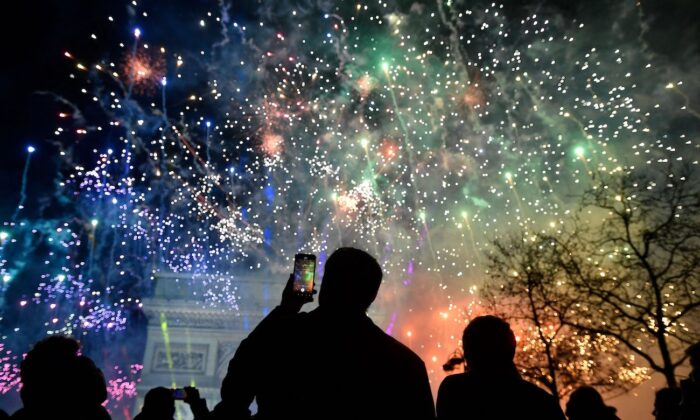 Un espectador sostiene un smartphone mientras estallan fuegos artificiales junto al Arco del Triunfo, en la avenida de los Campos Elíseos, durante las celebraciones de Año Nuevo en París, a primera hora del 1 de enero de 2023. (Julien de Rosa/AFP vía Getty Images)