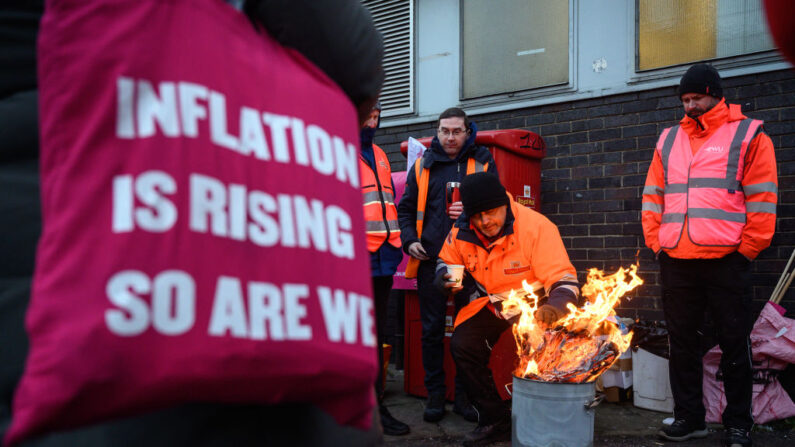 Un grupo de trabajadores postales en huelga se paran alrededor de un fuego mientras hacen manifestaciones por un aumento salarial frente a una oficina de clasificación de Royal Mail el 14 de diciembre de 2022 en Londres, Inglaterra. (Leon Neal/Getty Images)