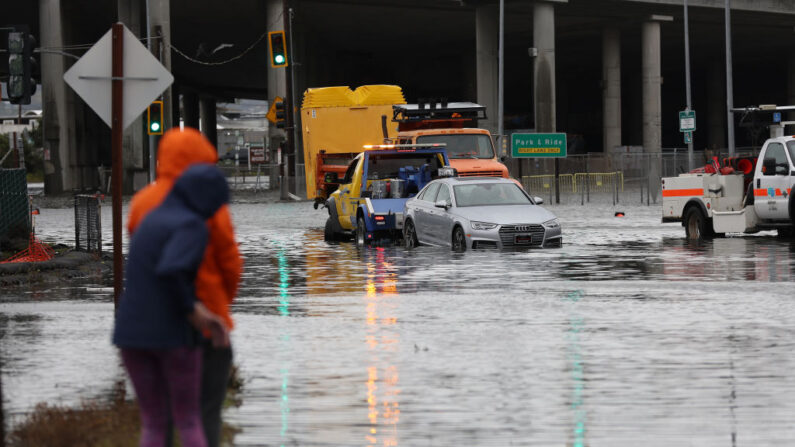 La gente mira como una grúa saca un coche de una intersección inundada el 04 de enero 2023 en Mill Valley, California. (Justin Sullivan/Getty Images)