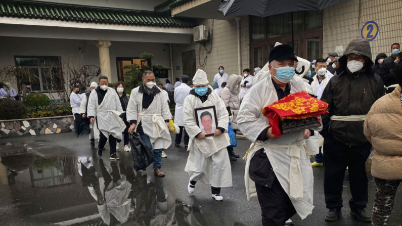 Un doliente lleva los restos incinerados de un ser querido mientras él y otros llevan ropa funeraria blanca tradicional, durante un funeral el 14 de enero de 2023 en Shanghái, China. (Kevin Frayer/Getty Images)