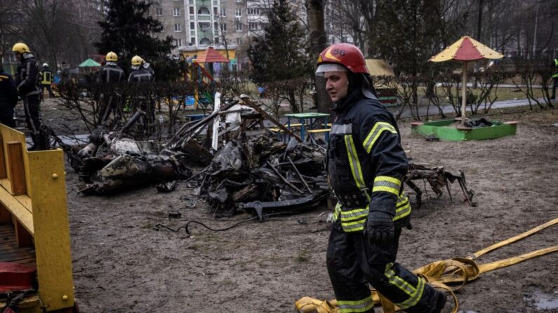 Los bomberos enrollan mangueras frente a los escombros mientras los trabajadores de los servicios de emergencia responden en el lugar donde se estrelló un helicóptero en Brovary, Ucrania, el 18 de enero de 2023. (Ed Ram/Getty Images)

