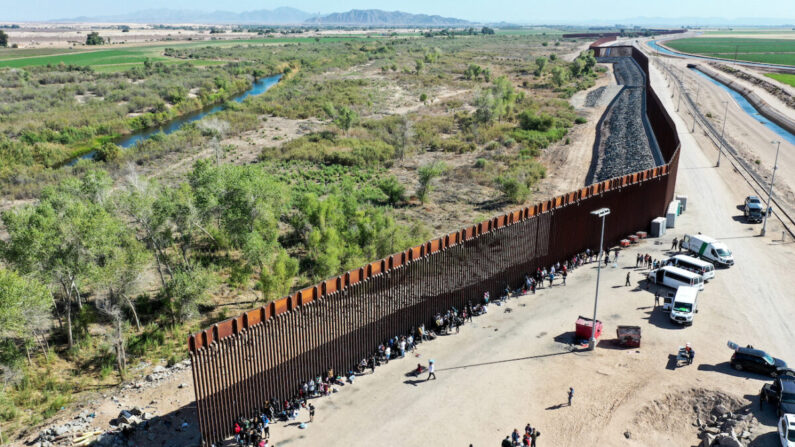 Inmigrantes ilegales esperan en fila para ser procesados por la Patrulla Fronteriza de Estados Unidos después de cruzar a través de una brecha en la barrera fronteriza entre Estados Unidos y México en Yuma, Arizona, el 21 de mayo de 2022. (Mario Tama/Getty Images)
