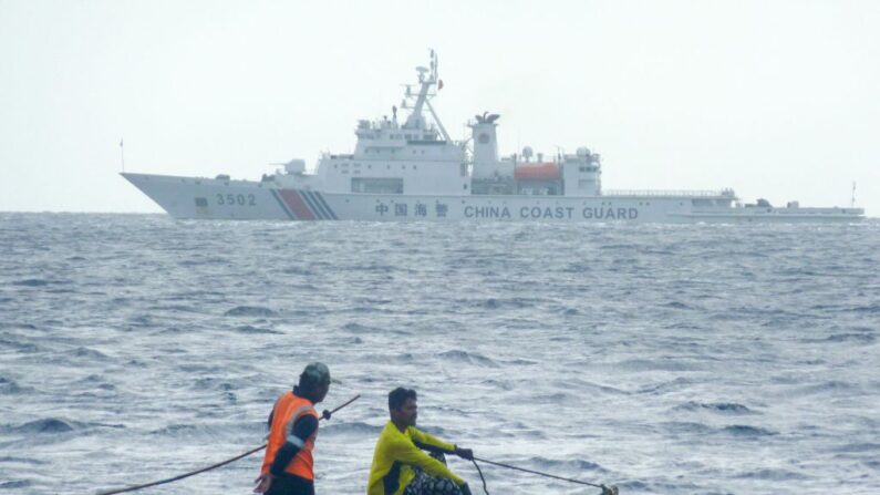 En esta foto tomada el 23 de diciembre de 2022, pescadores filipinos a bordo de su barco de madera navegan junto a un buque guardacostas chino en Scarborough Shoal, en el mar de China Meridional. (STR/AFP vía Getty Images)