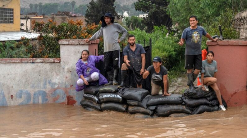 La gente mira detrás de sacos de arena como el agua inunda la principal carretera de acceso de Lima al interior del país en los Andes después de las fuertes lluvias en Chaclacayo, al este de Lima, Perú el 15 de marzo de 2023. (Cris Bouroncle/AFP vía Getty Images)