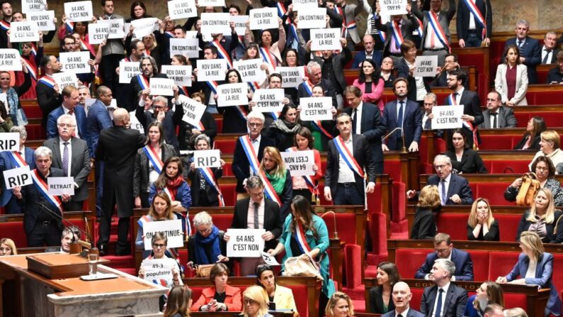 Miembros del grupo parlamentario de la Asamblea Nacional La France Insoumise (LFI) y de la coalición de izquierdas NUPES (Nueva Unión Ecológica y Social de los Pueblos) sostienen pancartas en las que se lee "64 es un no", "Nos vemos en la calle" junto a la primera ministra francesa Elisabeth Borne (1d) y el ministro de Trabajo francés Olivier Dussopt (2d) tras la votación de una moción de censura en la Asamblea Nacional francesa, el 20 de marzo de 2023. - (Bertrand Guay/AFP vía Getty Images)