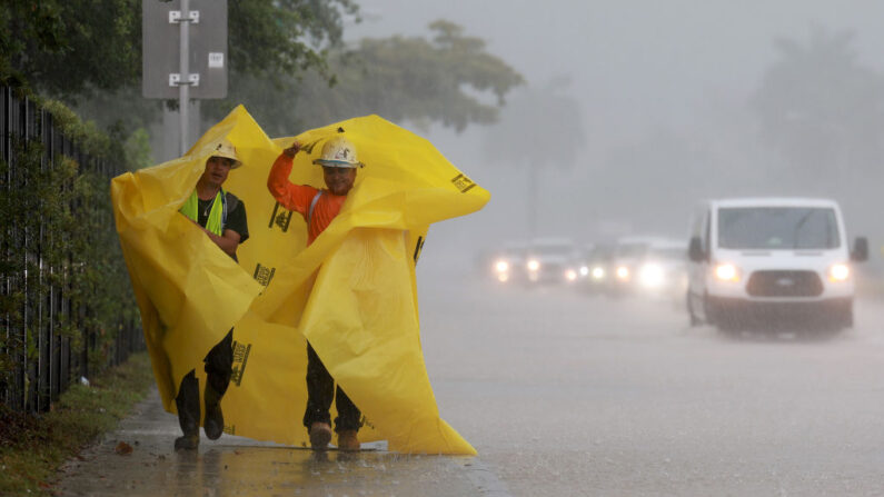Trabajadores utilizan una lona para protegerse de la lluvia el 12 de abril de 2023 en Dania Beach, Florida. (Joe Raedle/Getty Images)