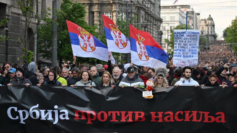 Manifestantes sostienen banderas serbias y una pancarta en la que se lee "Serbia contra la violencia" mientras marchan durante una concentración para pedir la dimisión de altos cargos y la reducción de la violencia en los medios de comunicación, pocos días después de que dos tiroteos consecutivos conmocionaran al país balcánico, en Belgrado, el 12 de mayo de 2023. (Andrej Isakovic/AFP vía Getty Images)
