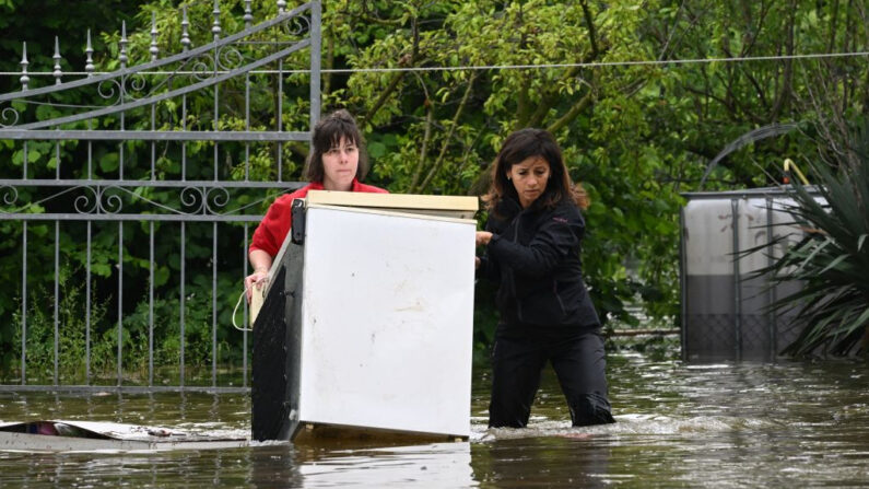 Vecinas sacan un electrodoméstico de una casa inundada el 20 de mayo de 2023 en el pueblo de Ghibullo, cerca de Rávena, tras la crecida de las aguas en la región de Emilia-Romaña (Italia). (Andreas Solaro/AFP vía Getty Images)