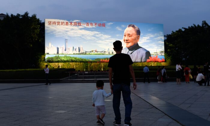 Un hombre sostiene la mano de un niño mientras caminan hacia un cartel del exlíder chino Deng Xiaoping en Shenzhen, en la provincia de Guangdong, en el sur de China, el 8 de noviembre de 2018. (Wang Zhao/AFP vía Getty Images)