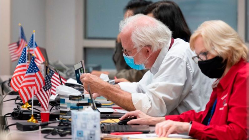 Un hombre comprueba el ID de un votante antes de darle una boleta en un centro de votación anticipada en Fairfax, Virginia, el 18 de septiembre de 2020. (ANDREW CABALLERO-REYNOLDS/AFP vía Getty Images)