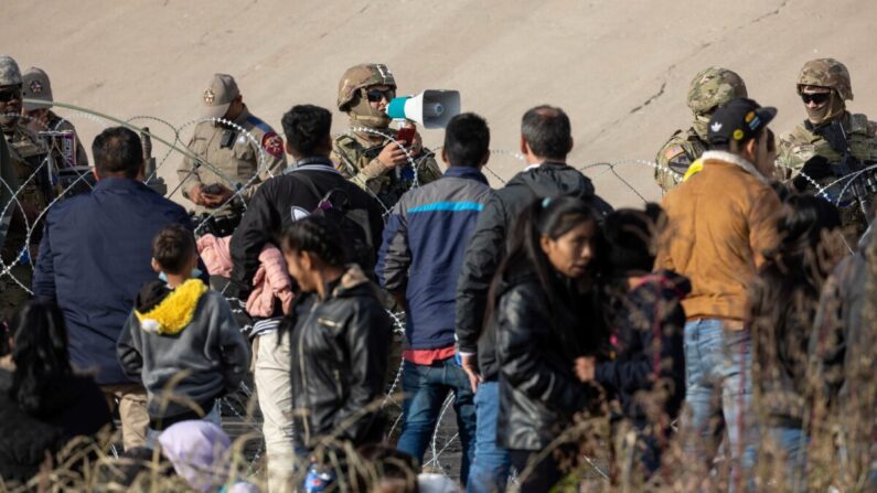 Un soldado de la Guardia Nacional de Texas habla con inmigrantes ilegales en una zona de paso fronterizo ilegal de alto tráfico a lo largo del Río Grande en El Paso, Texas, el 20 de diciembre de 2022. (John Moore/Getty Images)
