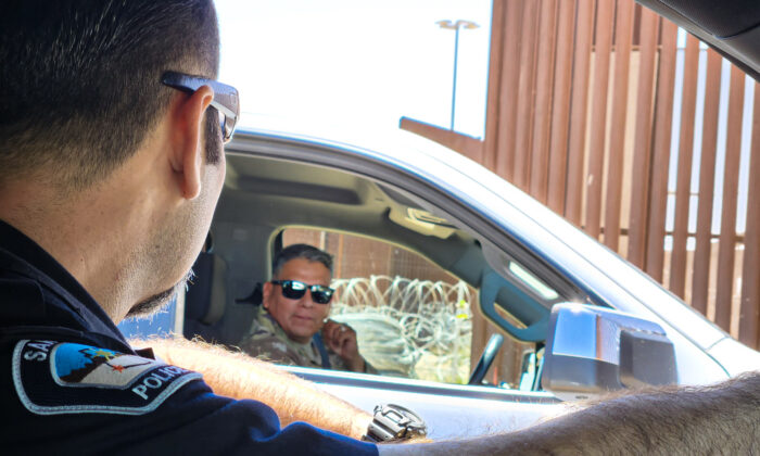 El teniente de policía de San Luis, Marco Santana (izq.), habla con un miembro de las fuerzas armadas estadounidenses en la valla fronteriza de San Luis, Arizona, el 4 de mayo de 2023. (Allan Stein/The Epoch Times)