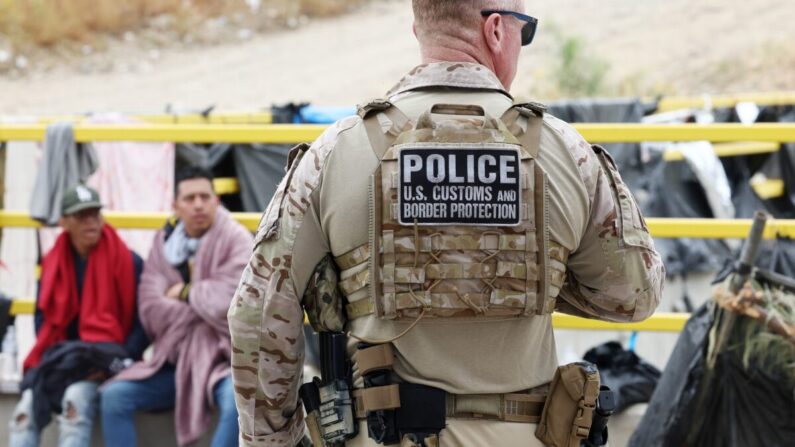 Un agente del Servicio de Aduanas y Protección de Fronteras vigila el traslado de inmigrantes desde un campamento improvisado entre los muros fronterizos entre Estados Unidos y México, en San Diego, el 13 de mayo de 2023. (Mario Tama/Getty Images)
