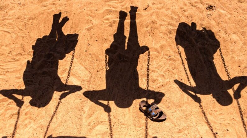 Las sombras de tres niños jugando en columpios el 7 de junio de 2022. (Badru Katumba/AFP vía Getty Images)
