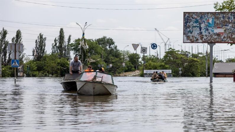 Residentes y trabajadores de los servicios de rescate usan barcas para moverse en una zona inundada de Jersón, Ucrania. EFE/Stas Kozliuk