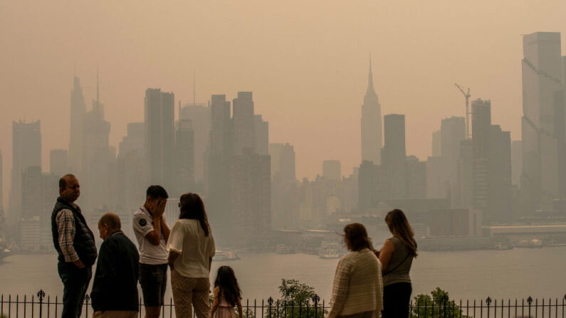Varias personas permanecen de pie en un parque el 7 de junio en Weehawken, Nueva Jersey, mientras el horizonte de la ciudad de Nueva York se cubre de bruma y humo procedentes de los incendios forestales de Canadá. (Eduardo Munoz Alvarez/Getty Images)