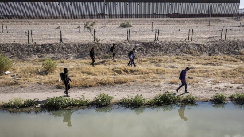 Inmigrantes hondureños caminan por el lado estadounidense del Río Grande y pasan por un campamento de inmigrantes vaciado después de cruzar de México a El Paso, Texas, el 13 de mayo de 2023. (John Moore/Getty Images)