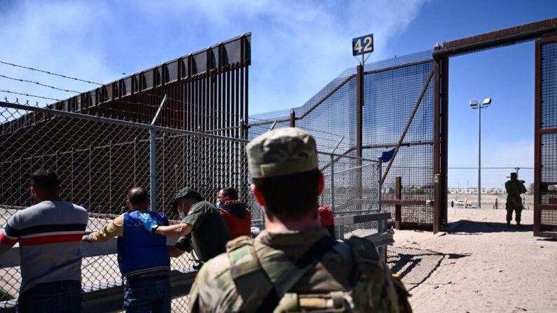 Un miembro de la Guardia Nacional del Ejército de Texas observa cómo un agente de la Patrulla Fronteriza de Aduanas y Protección de Fronteras de Estados Unidos registra a los migrantes tras entregarse para la tramitación de solicitudes de inmigración y asilo en la frontera entre Estados Unidos y México, en El Paso, Texas, el 10 de mayo de 2023. (PATRICK T. FALLON/AFP vía Getty Images)