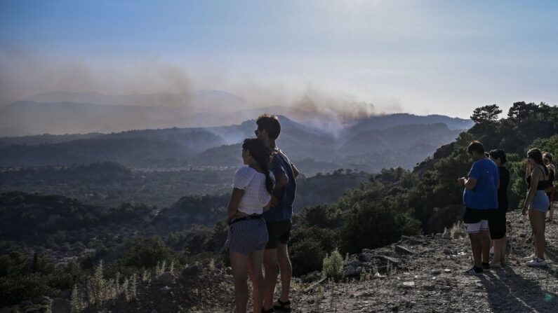 Residentes evacuados de los pueblos de Malonas y Masari en lo alto de una colina observando el fuego que se aproxima a sus pueblos en la isla griega de Rodas el 24 de julio de 2023. (Spyros Bakalis/AFP vía Getty Images)