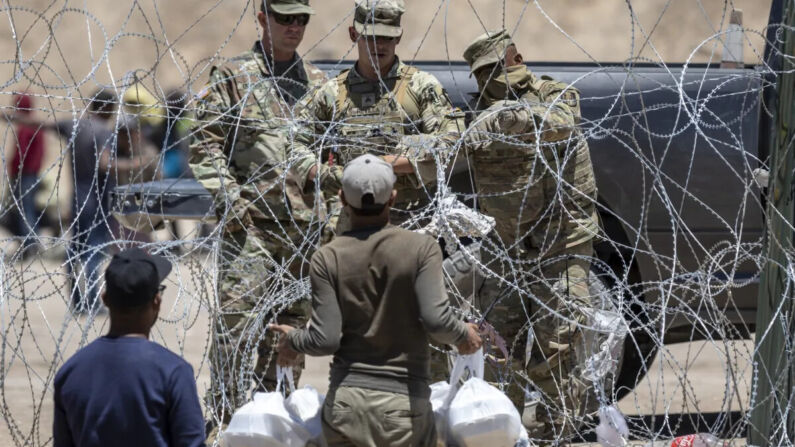 Soldados de la Guardia Nacional de Texas cierran una sección de alambre de púas que rodea un campamento de inmigrantes improvisado mientras un inmigrante intenta regresar con comida para su familia en El Paso, Texas, el 11 de mayo de 2023. (John Moore/Getty Images)