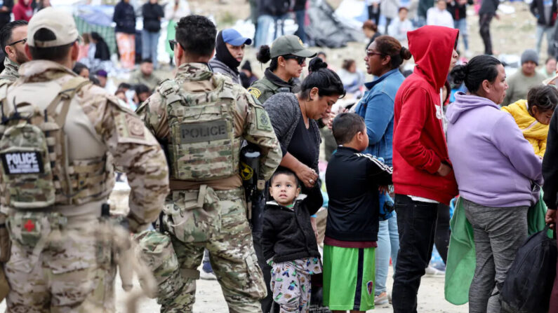 Agentes y oficiales federales de la ley vigilan mientras los inmigrantes hacen fila (derecha) para ser transportados desde un campamento improvisado entre EE.UU. y México, en San Diego, California, el 13 de mayo de 2023. (Mario Tama/Getty Images)
