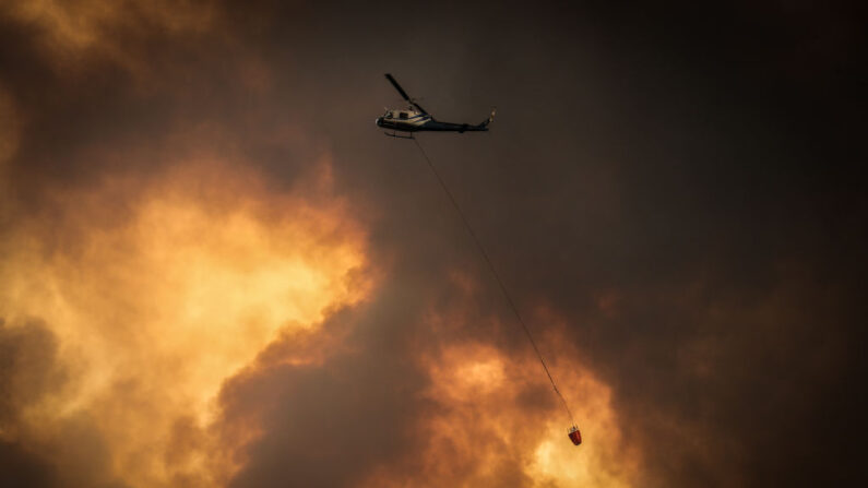 Helicópteros arrojan agua sobre incendios forestales mientras las llamas se acercan a las casas en una imagen de archivo. (David Gray/Getty Images)