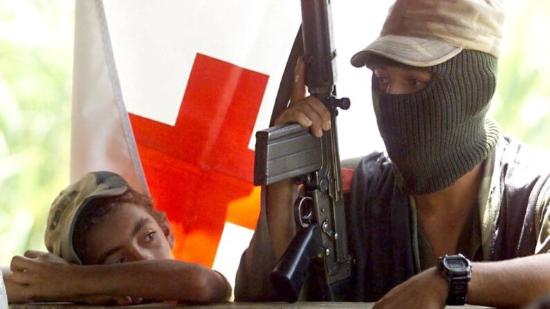 Un guerrillero colombiano del ELN (Ejército de Liberación Nacional) es observado por un niño de la localidad, 19 de septiembre, en un puesto de la Cruz Roja en la zona rural de La Quiebra, a unos 600 kms (372 millas), al noroeste de Bogotá. (PEDRO UGARTE/AFP via Getty Images)