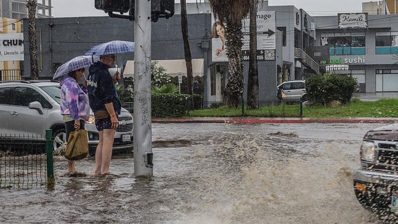 Una pareja sale de compras por una calle inundada en la ciudad de Tijuana (México). EFE/Joebeth Terriquez
