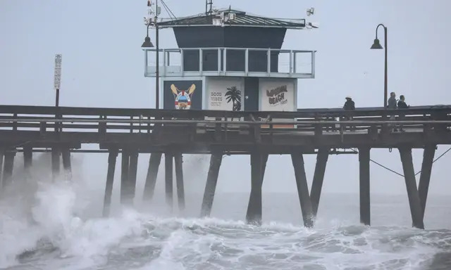 Varias personas permanecen en un muelle sobre el Océano Pacífico mientras la tormenta tropical Hilary se aproxima al condado de San Diego en Imperial Beach, California, el 20 de agosto de 2023. (Mario Tama/Getty Images)