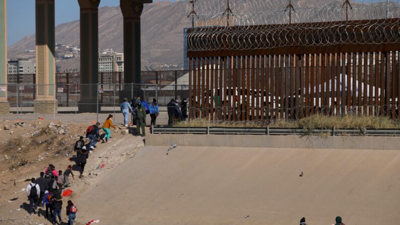 Migrantes esperan en fila para ser procesados por la Patrulla Fronteriza a lo largo del muro fronterizo después de cruzar el río Grande hacia El Paso, Texas, en la frontera entre México y Estados Unidos, visto desde Ciudad Juárez, estado de Chihuahua, México, el 19 de diciembre de 2022. (Herika Martinez/AFP vía Getty Images)