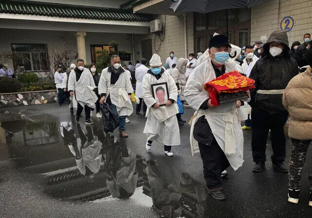 Un doliente lleva los restos incinerados de un ser querido mientras él y otros participantes llevan ropa funeraria blanca tradicional durante un funeral en Shanghai, China, el 14 de enero de 2023. (Kevin Frayer/Getty Images)