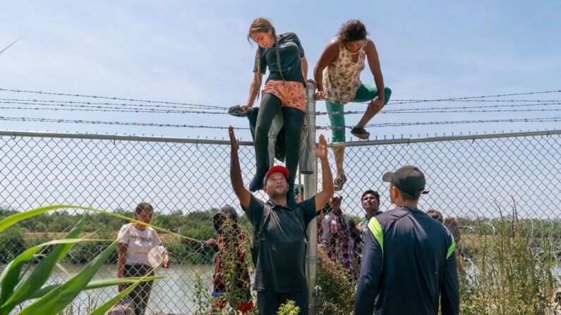 Migrantes se ayudan unos a otros a saltar una valla de alambre de espino para entrar en Estados Unidos desde México, en Eagle Pass, Texas, el 25 de agosto de 2023. (Suzanne Cordeiro/AFP/Getty Images)