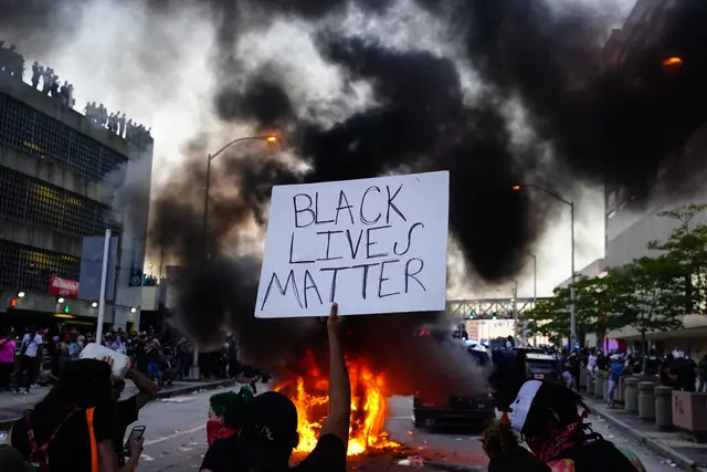 Un hombre sostiene un cartel de Black Lives Matter mientras un coche de policía arde frente a él durante una protesta por la muerte en Minneapolis de George Floyd mientras estaba bajo custodia policial, frente al CNN Center de Atlanta el 29 de mayo de 2020. (Elijah Nouvelage/Getty Images)
