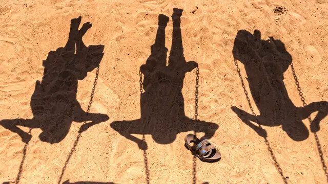 Las sombras de tres niños jugando en columpios el 7 de junio de 2022. (Badru Katumba/AFP vía Getty Images)