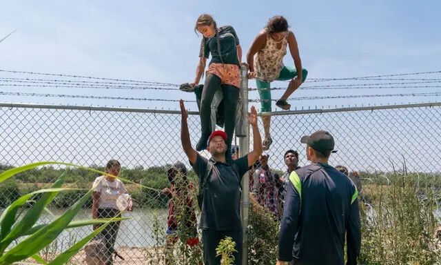 Inmigrantes ilegales se ayudan unos a otros a saltar una valla de alambre de púas para entrar en Estados Unidos desde México, en Eagle Pass, Texas, el 25 de agosto de 2023. (Suzanne Cordeiro/AFP vía Getty Images)