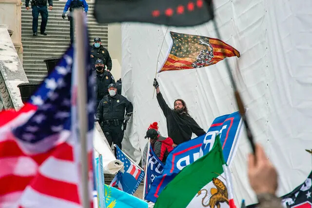 Un hombre agita una bandera desde las escaleras del Capitolio de Estados Unidos después de romper una línea policial mientras manifestantes y partidarios del presidente estadounidense Donald Trump se reúnen fuera del edificio el 6 de enero de 2021. (Joseph Prezioso/AFP vía Getty Images)
