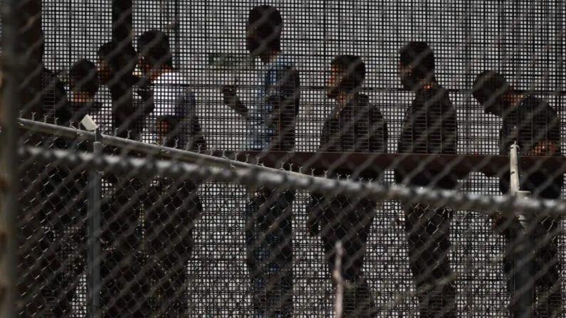 Inmigrantes ilegales esperan a lo largo del muro fronterizo para abordar un autobús después de entregarse a los agentes de la Patrulla Fronteriza de Aduanas y Protección Fronteriza (CBP) de Estados Unidos, en la frontera entre Estados Unidos y México, en El Paso, Texas, el 12 de mayo de 2023. (Patrick T. Fallon/AFP vía Getty Images)
