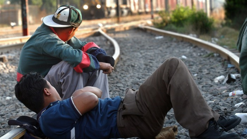 Dos inmigrantes esperan sobre las vías para montarse en un tren con destino a la frontera entre México y Estados Unidos. Imagen de archivo. (EFE/David de la Paz)
