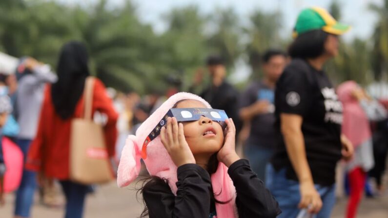 Una niña usa gafas con filtro solar para observar la luna mientras se mueve frente al sol en un raro eclipse solar de "anillo de fuego" en Tanjung Piai, Malasia, el 26 de diciembre de 2019. (Sadiq Asyraf/AFP vía Getty Images)