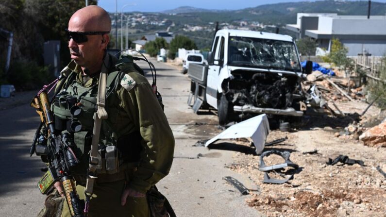 En esta imagen tomada durante una gira de medios organizada por el ejército israelí, un soldado israelí habla junto a un coche dañado cerca de la frontera con Líbano el 21 de octubre de 2023. (Yuri Cortez/AFP vía Getty Images)