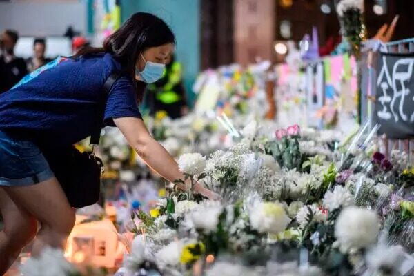 Los dolientes presentan sus respetos junto a flores y una pancarta que dice "De todos nosotros, Dios bendiga a Chow Tsz-Lok" en el lugar donde el estudiante Alex Chow, de 22 años, cayó durante una protesta reciente en Kowloon, Hong Kong, el 8 de noviembre del 2019. (Anthony Wallace/AFP vía Getty Images)