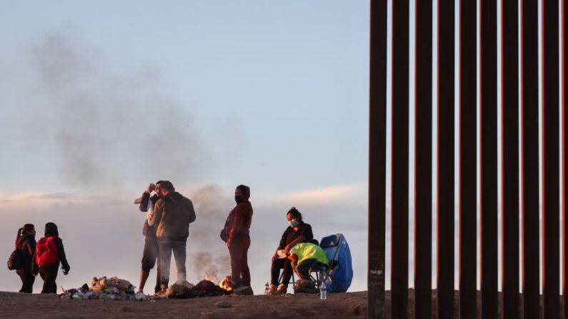 Migrantes de Ecuador se calientan junto a un fuego después del amanecer a lo largo de una brecha en la barrera fronteriza entre Estados Unidos y México, mientras esperan ser procesados por la Patrulla Fronteriza de Estados Unidos, después de cruzar desde México el 22 de mayo de 2022 en Yuma, Arizona. (Mario Tama/Getty Images)