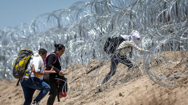 Inmigrantes ilegales caminan a través del alambre de púas que rodea un campamento improvisado de migrantes después de cruzar la frontera desde México, en El Paso, Texas, el 11 de mayo de 2023. (John Moore/Getty Images)
